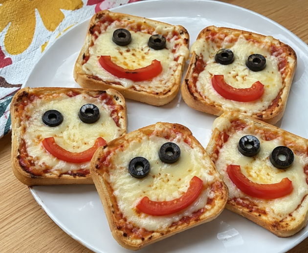 Mini pizzas de pan de caja con queso derretido y caritas sonrientes de aceitunas y jitomate