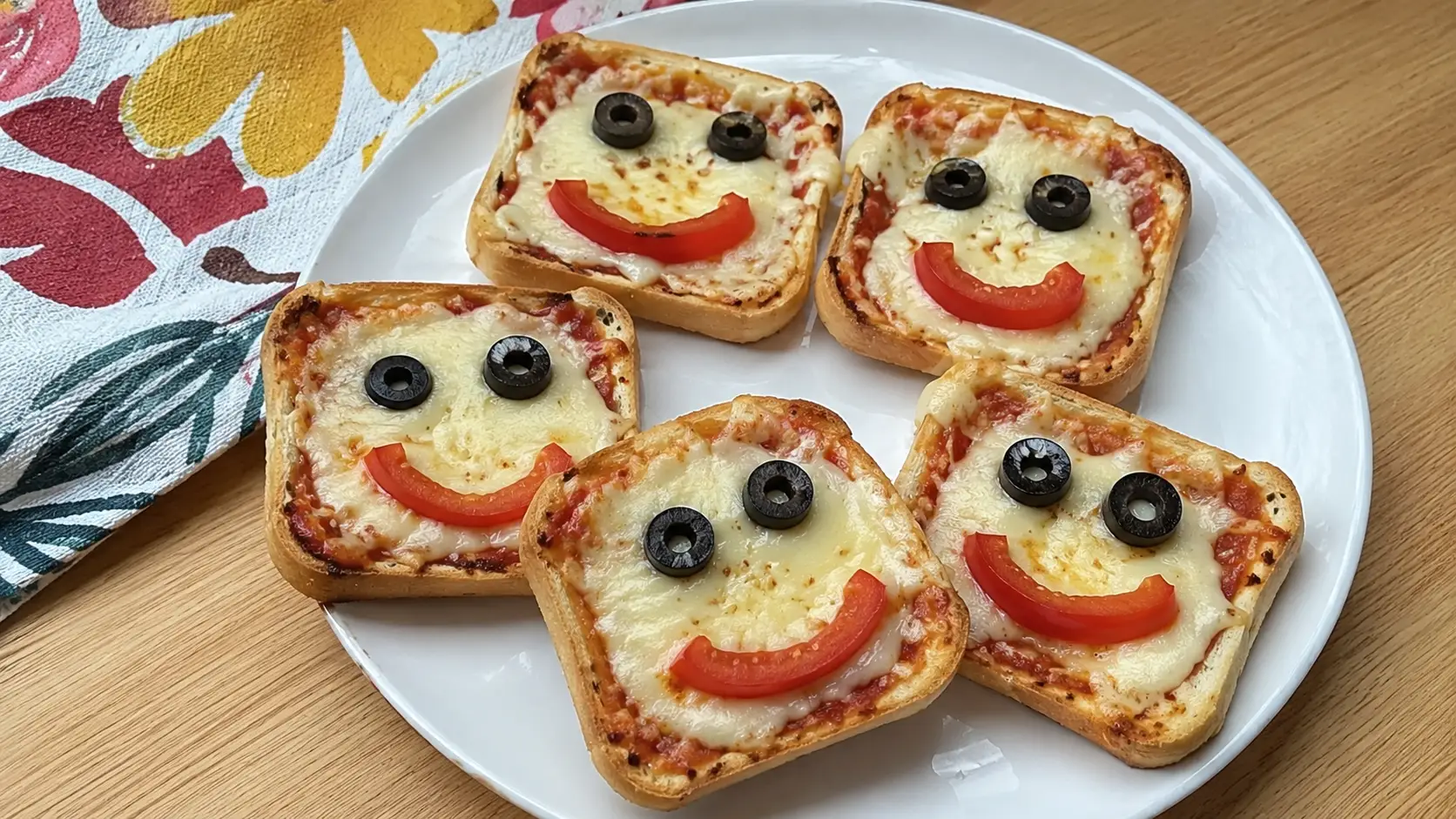 Mini pizzas de pan de caja con queso derretido y caritas sonrientes de aceitunas y jitomate