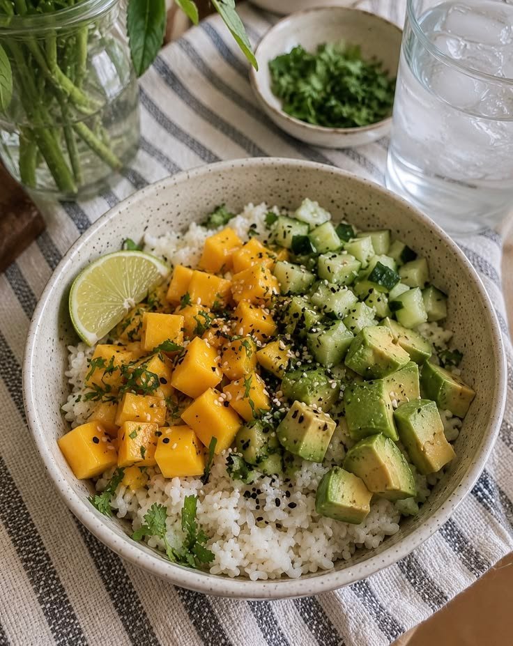 Bowl fresco de arroz con cubos de mango, aguacate y pepino, ajonjolí y cilantro, con una rodaja de limón