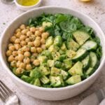 Bowl verde de espinaca con garbanzos, aguacate en cubos y pepino, con aderezo de limón y un gajo de limón al lado