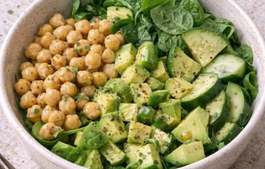 Bowl verde de espinaca con garbanzos, aguacate en cubos y pepino, con aderezo de limón y un gajo de limón al lado