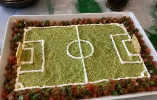 Guacamole en forma de cancha de fútbol con líneas de crema, borde de pico de gallo y porterías de totopos, botana para el Mundial