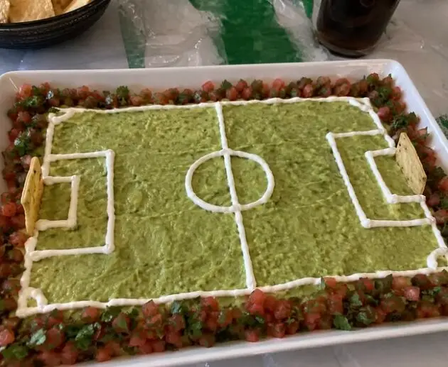 Guacamole en forma de cancha de fútbol con líneas de crema, borde de pico de gallo y porterías de totopos, botana para el Mundial