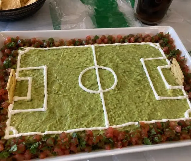 Guacamole en forma de cancha de fútbol con líneas de crema, borde de pico de gallo y porterías de totopos, botana para el Mundial
