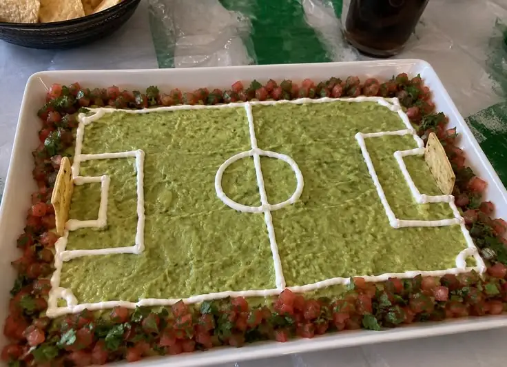 Guacamole en forma de cancha de fútbol con líneas de crema, borde de pico de gallo y porterías de totopos, botana para el Mundial