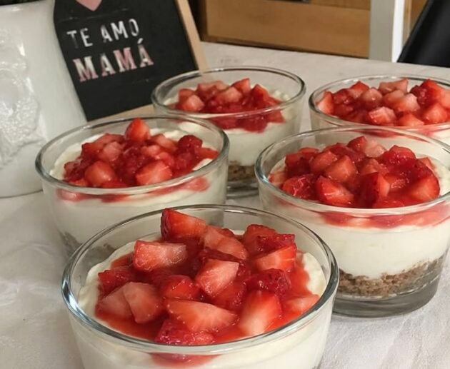 Mini cheesecakes de fresa en vasos con base de galleta, relleno cremoso blanco y fresas picadas encima