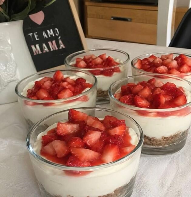 Mini cheesecakes de fresa en vasos con base de galleta, relleno cremoso blanco y fresas picadas encima