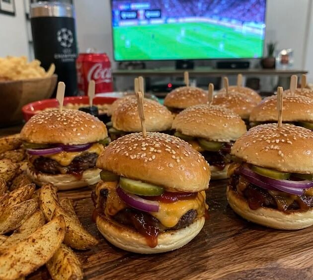 Mini hamburguesas BBQ con queso cheddar gratinado, pepinillos y cebolla morada atravesadas con palillo, servidas con papas en gajos para ver fútbol