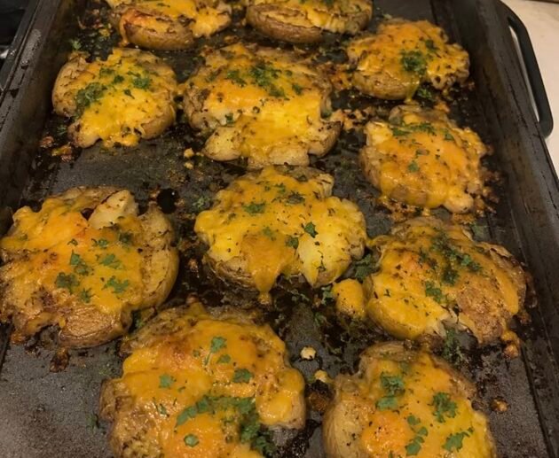 Papas smash crujientes al horno cubiertas con queso derretido y perejil fresco sobre una charola metálica