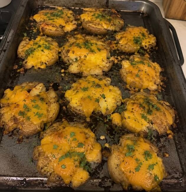 Papas smash crujientes al horno cubiertas con queso derretido y perejil fresco sobre una charola metálica