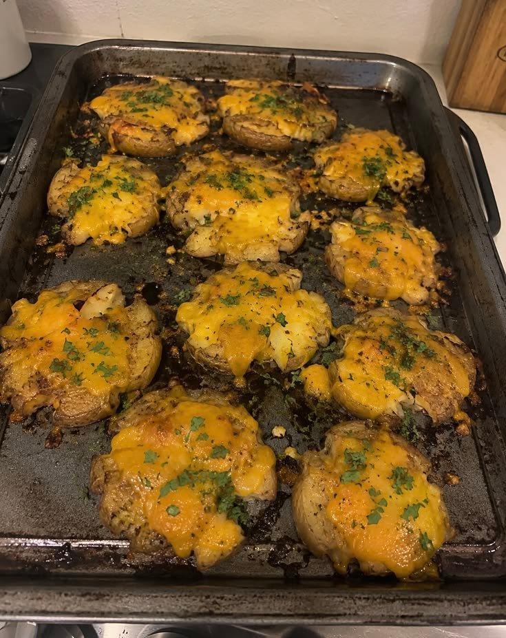 Papas smash crujientes al horno cubiertas con queso derretido y perejil fresco sobre una charola metálica