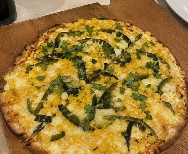 Pizza fácil de elote y rajas de chile poblano con queso mozzarella derretido y cilantro fresco sobre una tabla de madera
