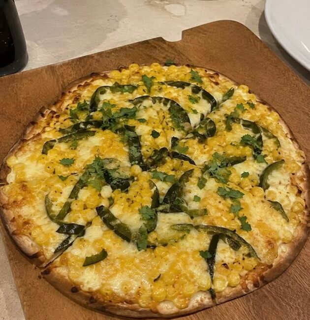 Pizza fácil de elote y rajas de chile poblano con queso mozzarella derretido y cilantro fresco sobre una tabla de madera