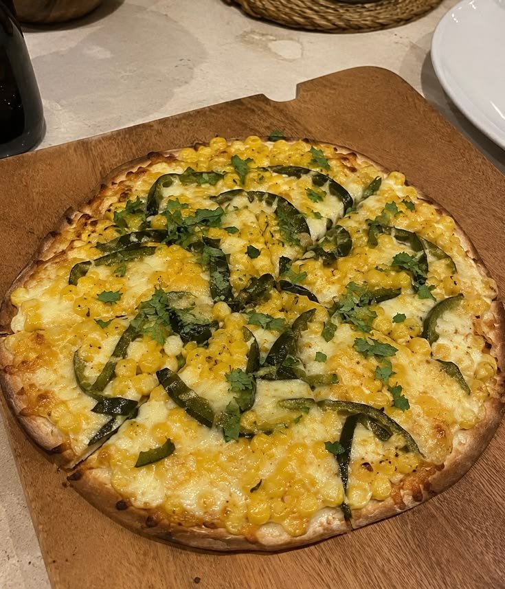 Pizza fácil de elote y rajas de chile poblano con queso mozzarella derretido y cilantro fresco sobre una tabla de madera
