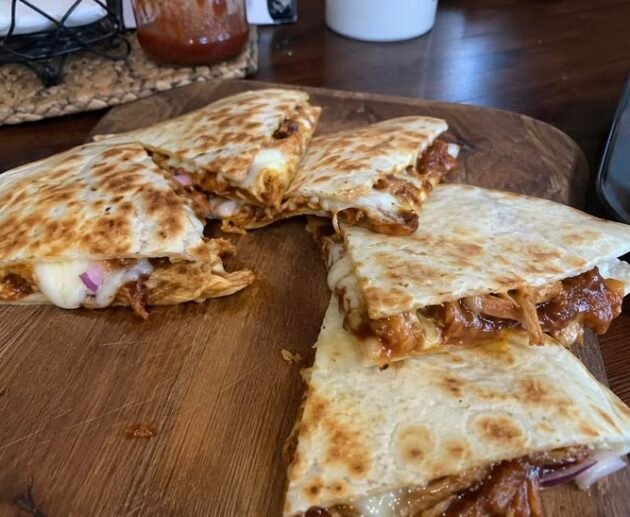 Quesadillas de pollo BBQ doradas y crujientes cortadas en triángulos con queso derretido y cebolla morada sobre una tabla de madera
