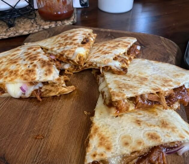 Quesadillas de pollo BBQ doradas y crujientes cortadas en triángulos con queso derretido y cebolla morada sobre una tabla de madera