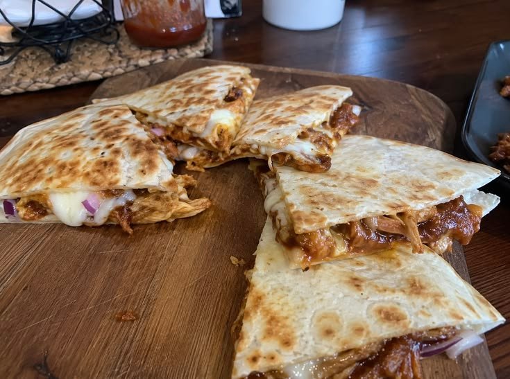 Quesadillas de pollo BBQ doradas y crujientes cortadas en triángulos con queso derretido y cebolla morada sobre una tabla de madera