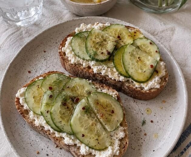 Tostadas de pan rústico con ricotta y rodajas finas de pepino, aceite de oliva y hojuelas de chile, servidas en un plato
