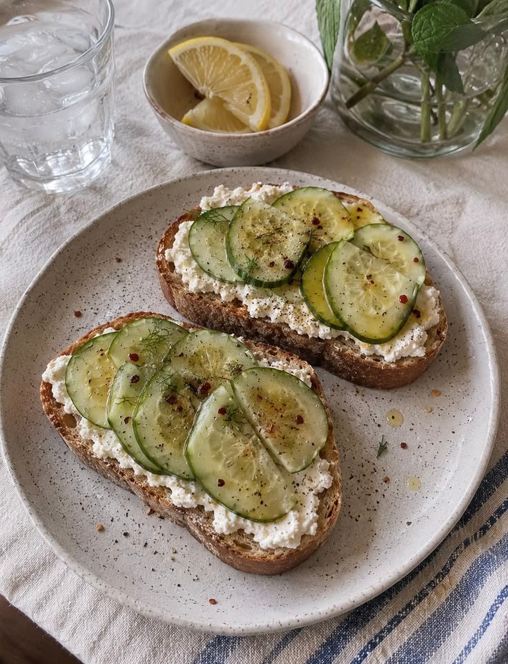 Tostadas de pan rústico con ricotta y rodajas finas de pepino, aceite de oliva y hojuelas de chile, servidas en un plato