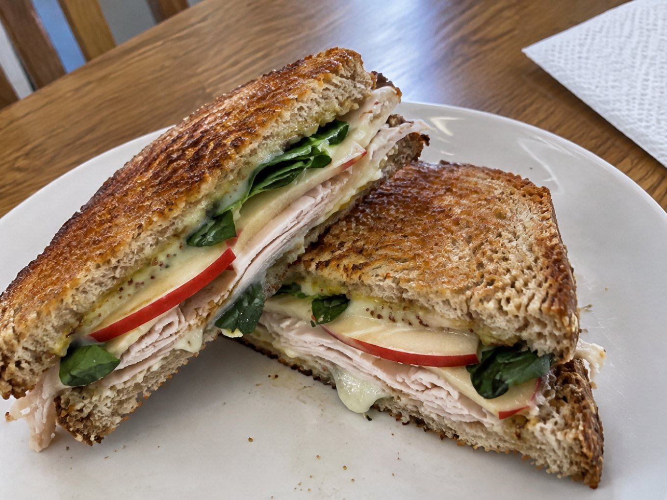 Sándwich tostado de pavo, manzana y queso derretido cortado en diagonal sobre plato blanco, receta saludable y fácil para el lunch