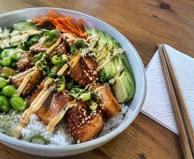 Bowl de salmón teriyaki saludable con arroz, edamame, pepino, aguacate y ajonjolí sobre mesa de madera, receta fácil en 25 minutos