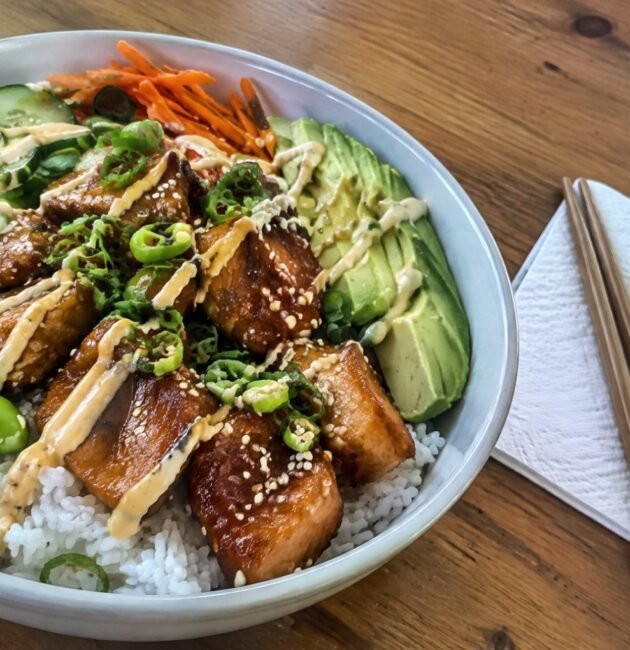 Bowl de salmón teriyaki saludable con arroz, edamame, pepino, aguacate y ajonjolí sobre mesa de madera, receta fácil en 25 minutos