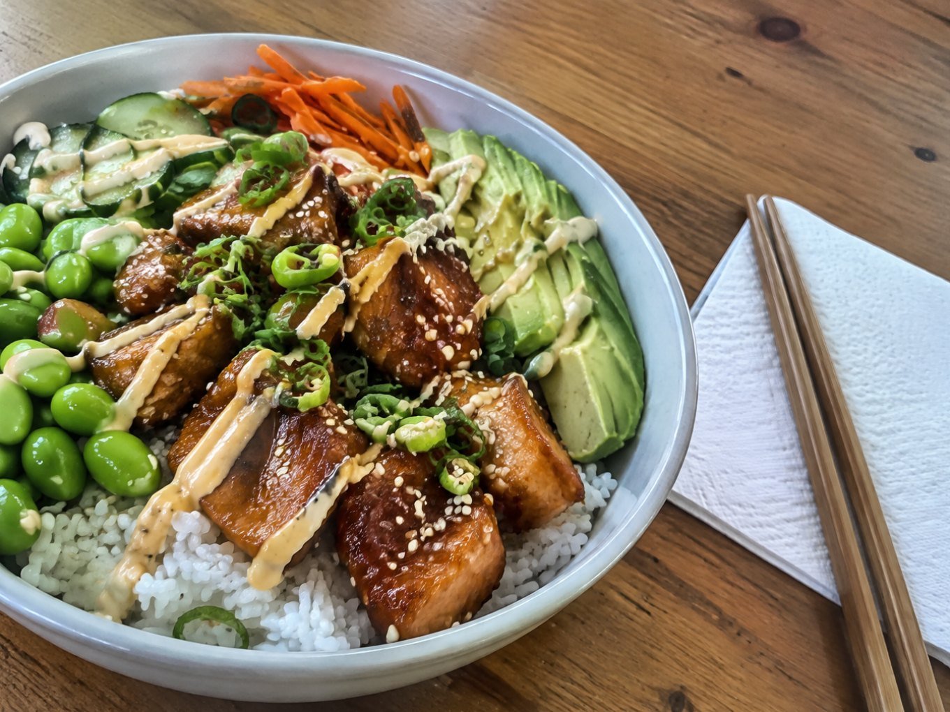 Bowl de salmón teriyaki saludable con arroz, edamame, pepino, aguacate y ajonjolí sobre mesa de madera, receta fácil en 25 minutos