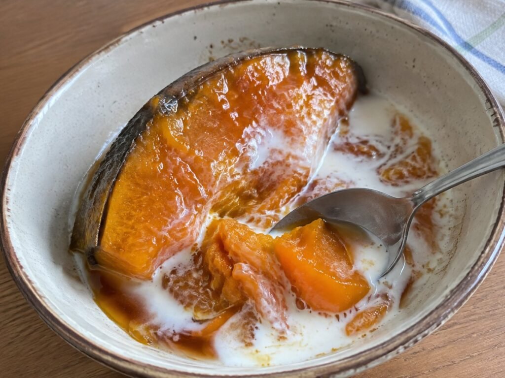 Porción de calabaza en tacha en tazón con un chorrito de leche fría mezclándose con el almíbar oscuro de piloncillo y una cuchara