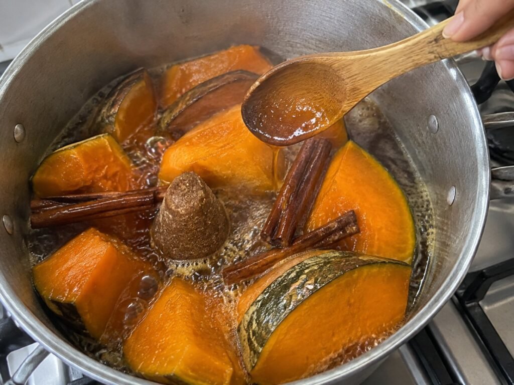 Gajos de calabaza de castilla cociéndose en olla con piloncillo derretido y rajas de canela mientras se bañan con almíbar con cuchara