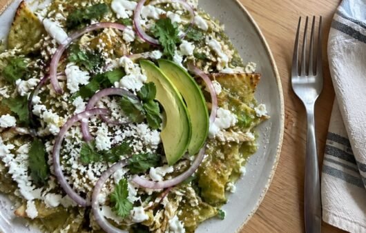 Plato de chilaquiles verdes horneados con pollo deshebrado, crema, queso fresco, cebolla morada y aguacate visto desde arriba