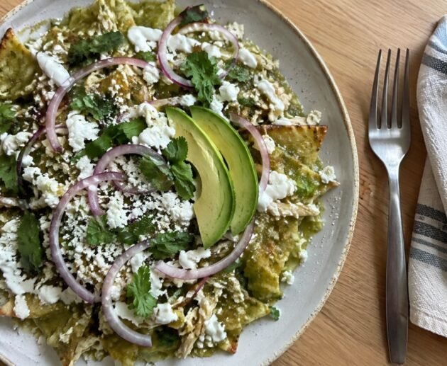 Plato de chilaquiles verdes horneados con pollo deshebrado, crema, queso fresco, cebolla morada y aguacate visto desde arriba