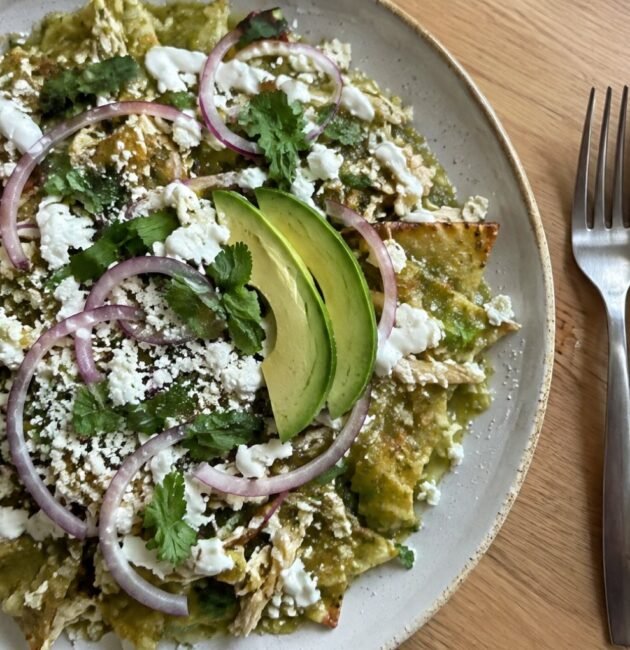 Plato de chilaquiles verdes horneados con pollo deshebrado, crema, queso fresco, cebolla morada y aguacate visto desde arriba