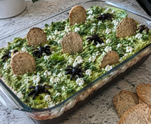 Dip de frijol negro en capas con guacamole, yogur al chipotle y totopos horneados en forma de lápida, botana de Halloween saludable