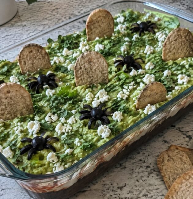 Dip de frijol negro en capas con guacamole, yogur al chipotle y totopos horneados en forma de lápida, botana de Halloween saludable