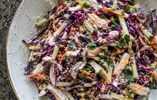 Ensalada crujiente de col morada, manzana verde, pollo deshebrado y zanahoria con aderezo cremoso de yogur y limón en tazón de cerámica