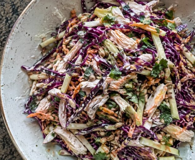 Ensalada crujiente de col morada, manzana verde, pollo deshebrado y zanahoria con aderezo cremoso de yogur y limón en tazón de cerámica