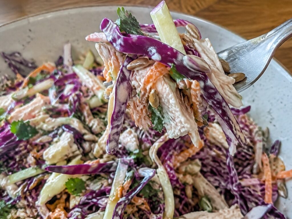 Tenedor con un bocado de ensalada de col morada, manzana verde y pollo deshebrado cubiertos de aderezo de yogur y limón