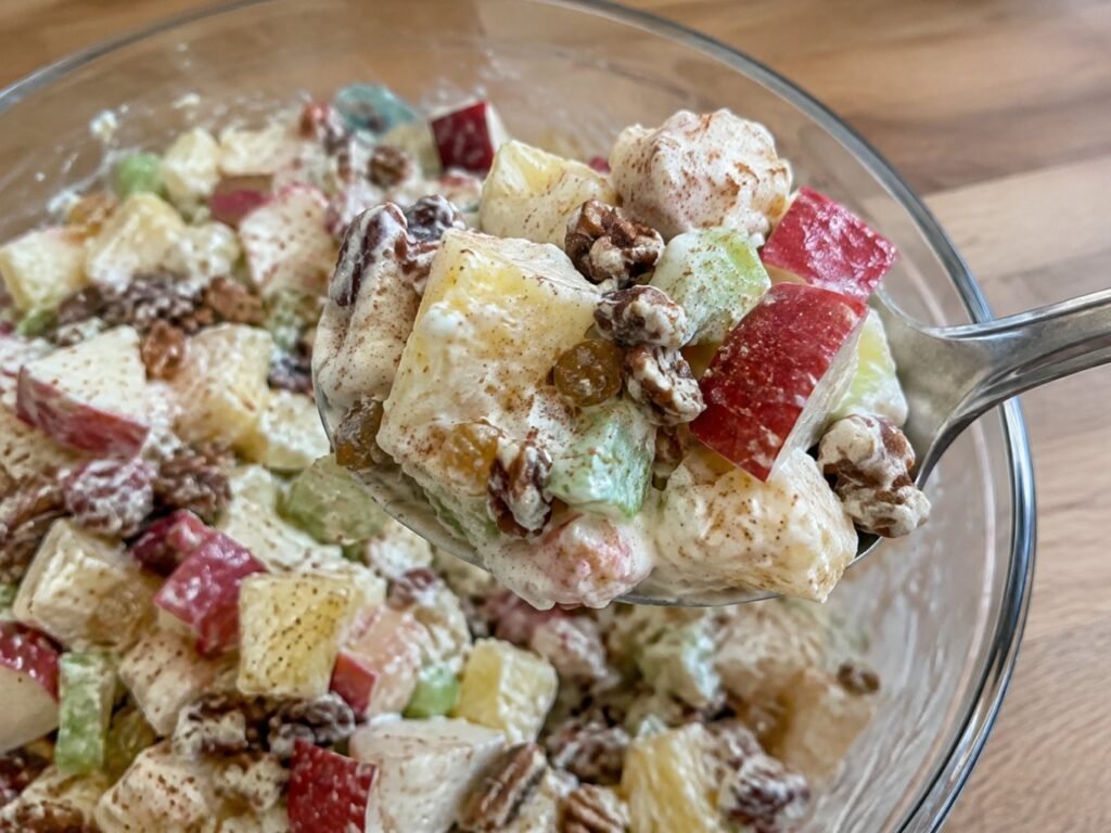 Cuchara sirviendo ensalada de manzana cremosa con yogur griego, cubos de manzana roja con cáscara y nuez pecana crujiente