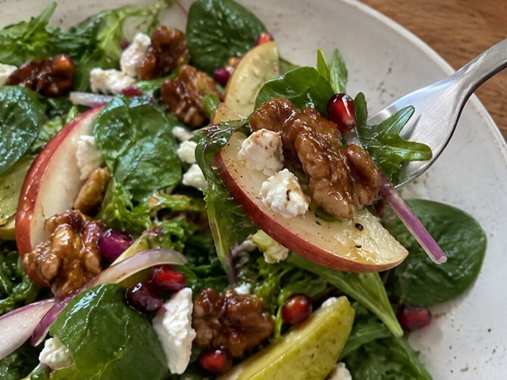 Tenedor levantando un bocado de ensalada con rebanada de pera, queso de cabra desmoronado y nuez caramelizada brillante, receta saludable fácil