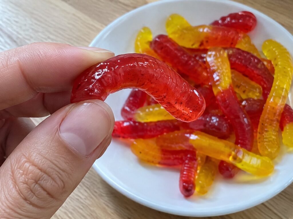 Mano doblando una gomita roja de fresa en forma de gusanito que muestra su textura brillante de gelatina de fruta con agar-agar