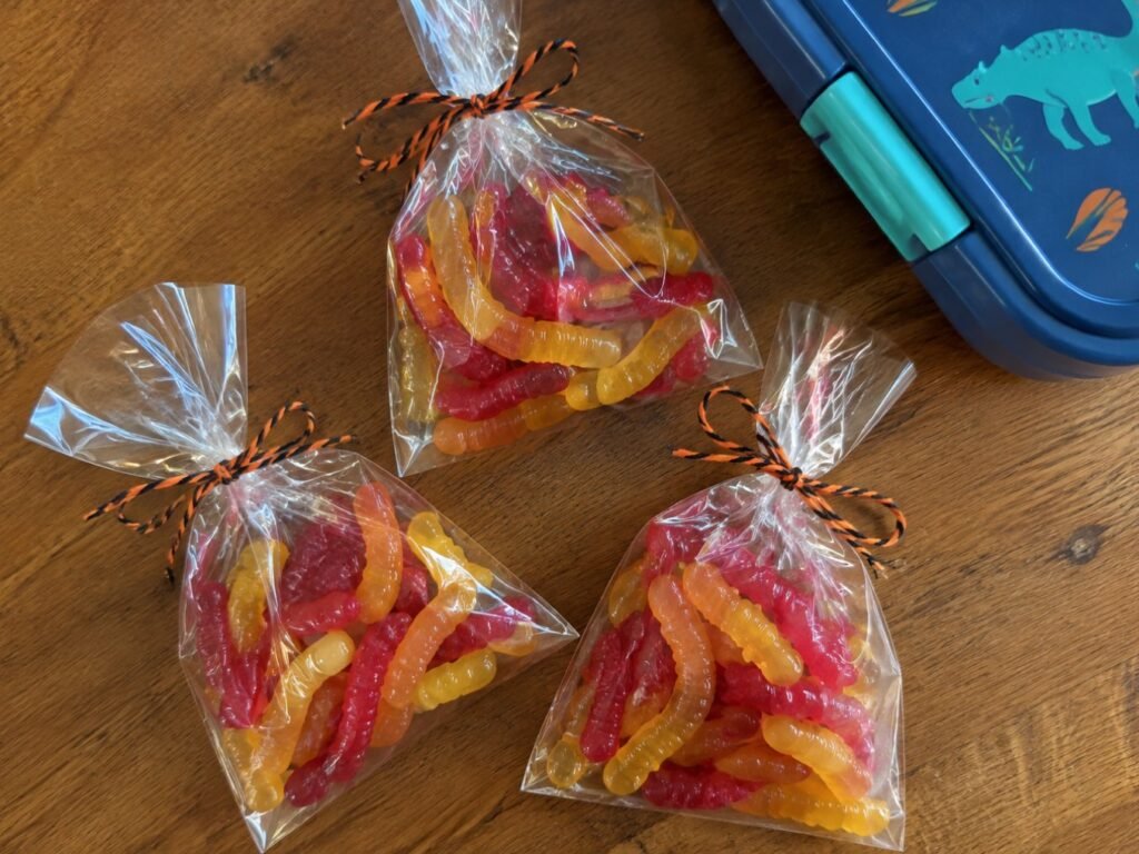 Bolsitas transparentes con gomitas caseras de fresa y mango atadas con cordón naranja y negro junto a una lonchera infantil