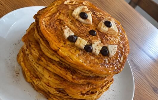 Torre de hot cakes de calabaza y avena con carita de Halloween de plátano y chocolate amargo, desayuno saludable y fácil para niños