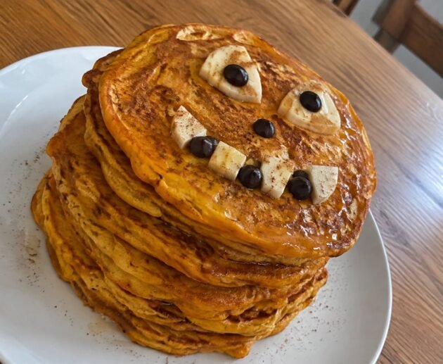 Torre de hot cakes de calabaza y avena con carita de Halloween de plátano y chocolate amargo, desayuno saludable y fácil para niños
