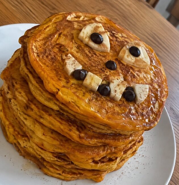 Torre de hot cakes de calabaza y avena con carita de Halloween de plátano y chocolate amargo, desayuno saludable y fácil para niños
