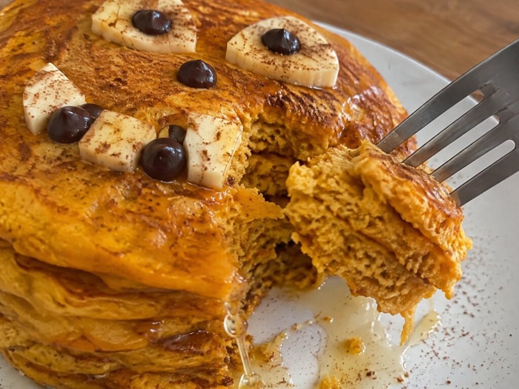 Tenedor cortando un bocado de hot cakes de calabaza y avena esponjosos con miel escurriendo, desayuno de otoño saludable