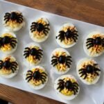 Charola de huevos rellenos araña con aceitunas negras y paprika, botana de Halloween fácil y alta en proteína sobre barra de cocina