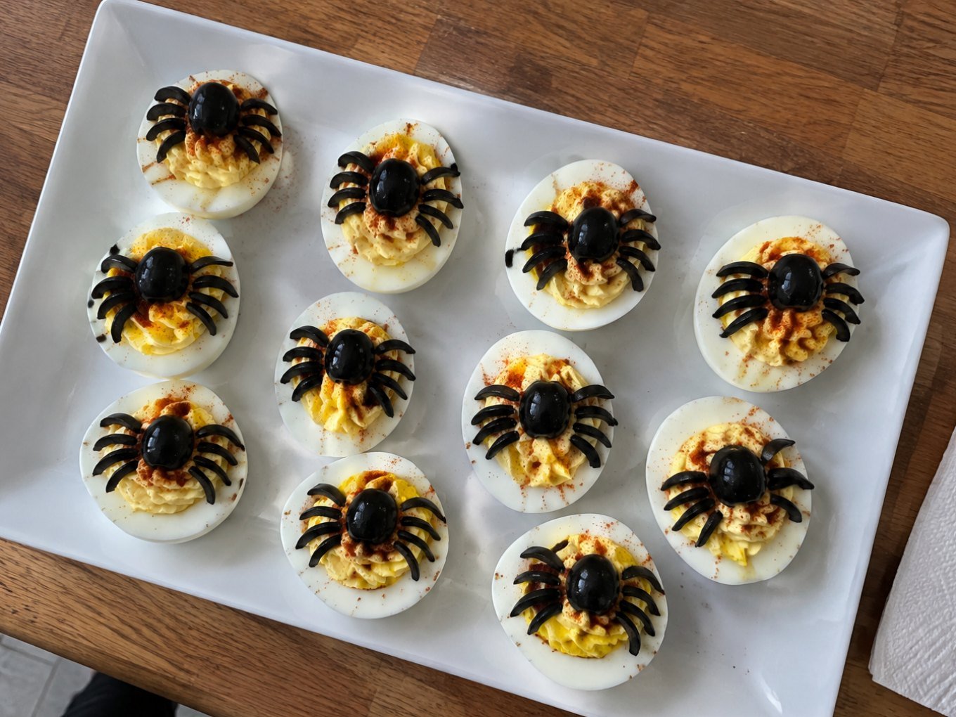 Charola de huevos rellenos araña con aceitunas negras y paprika, botana de Halloween fácil y alta en proteína sobre barra de cocina