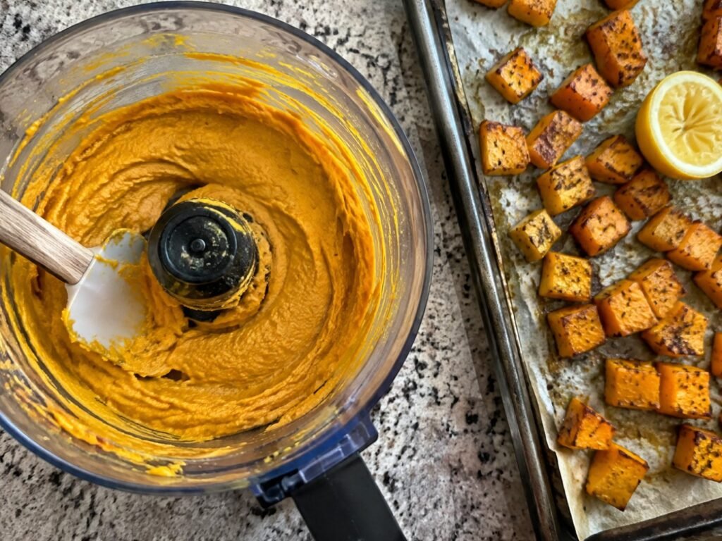 Hummus de calabaza recién procesado en el procesador de alimentos junto a una charola de calabaza asada y limón, paso a paso fácil