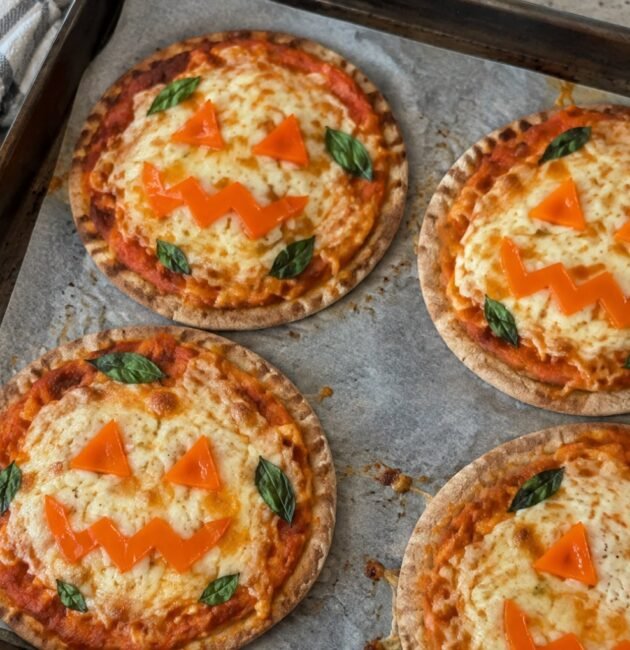 Mini pizzas de Halloween en pan pita integral con salsa de calabaza, mozzarella gratinada y caritas de pimiento naranja en charola casera