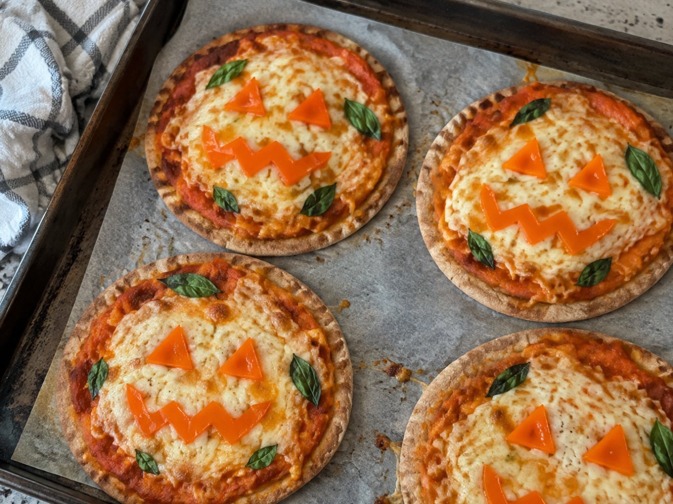Mini pizzas de Halloween en pan pita integral con salsa de calabaza, mozzarella gratinada y caritas de pimiento naranja en charola casera